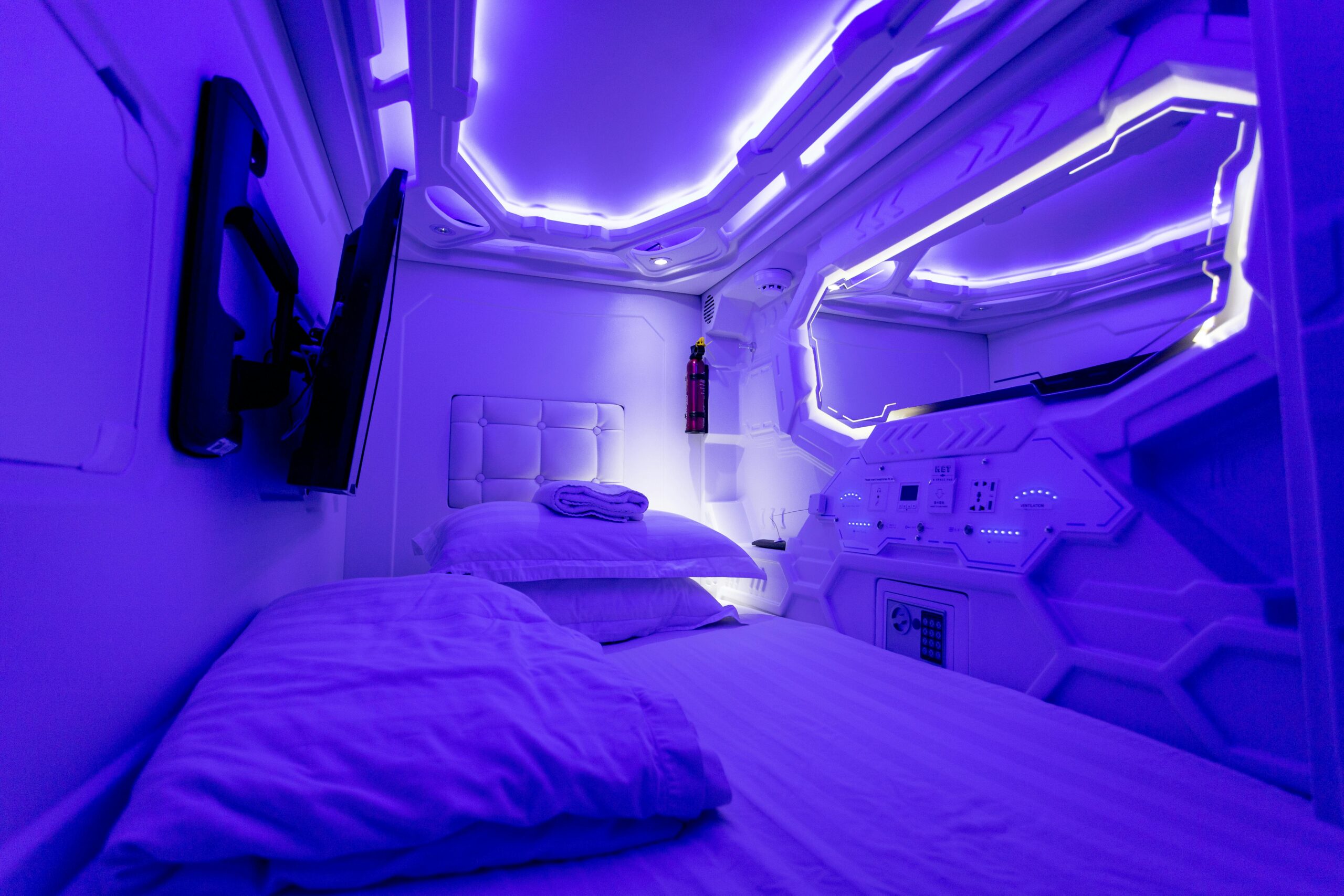 Explore a futuristic capsule hotel room adorned with calming ultraviolet lighting, perfect for a tranquil stay.